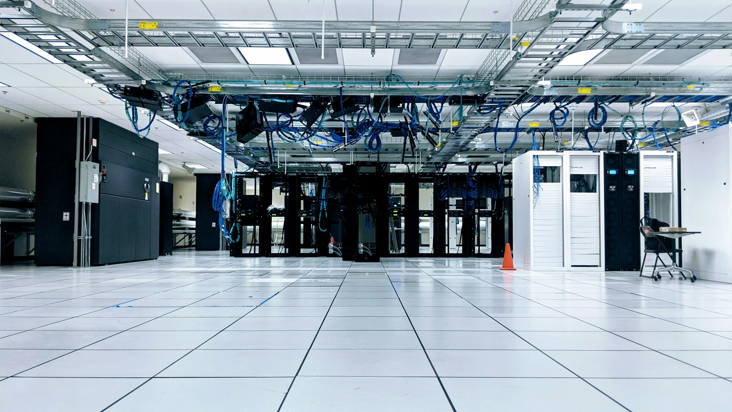 Wide view of a data center hall with overhead cable management and raised floor
